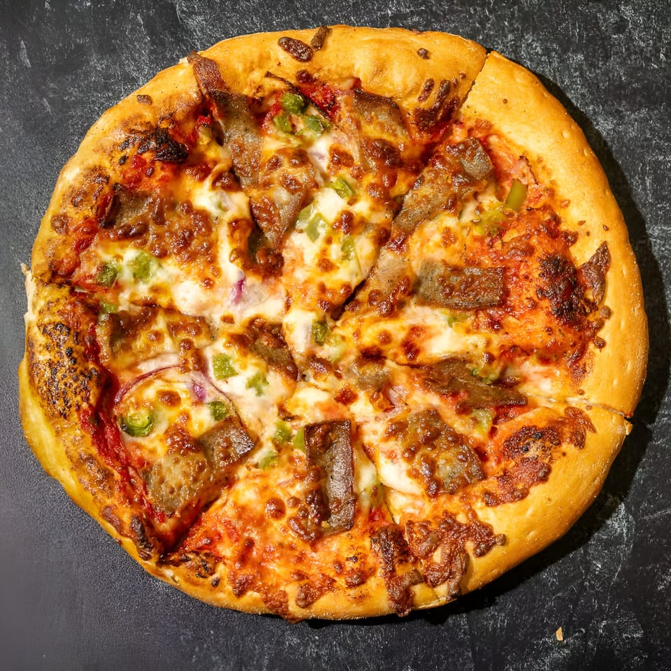Overhead view of a Mizan Pizza with meat, green peppers, and onions on a dark surface.
