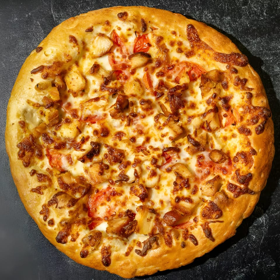 Mizan Pizza's chicken pizza, topped with melted cheese, chicken pieces, and diced tomatoes on a dark surface.