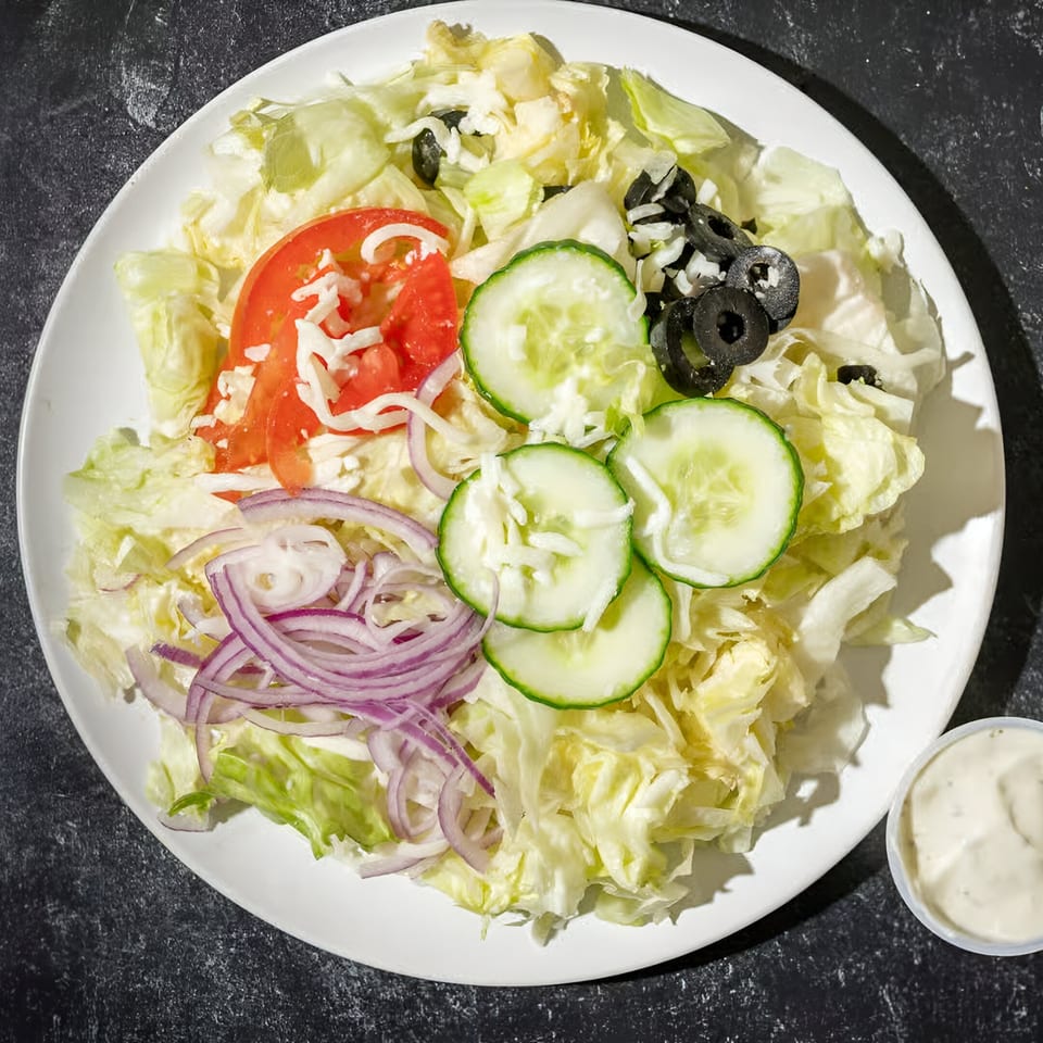 A fresh Mizan Pizza side salad with lettuce, tomatoes, cucumbers, red onions, olives, and dressing.