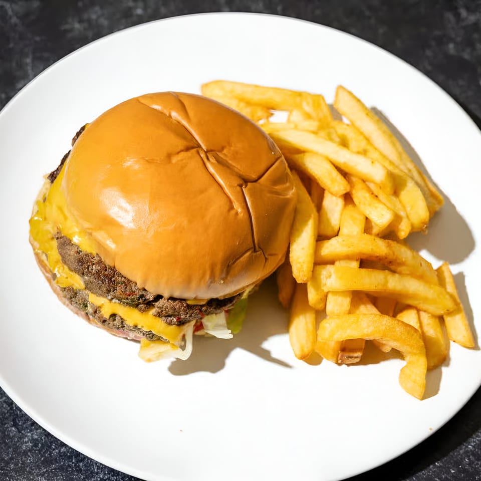 A double cheeseburger with melted cheese and a side of golden french fries on a white plate.